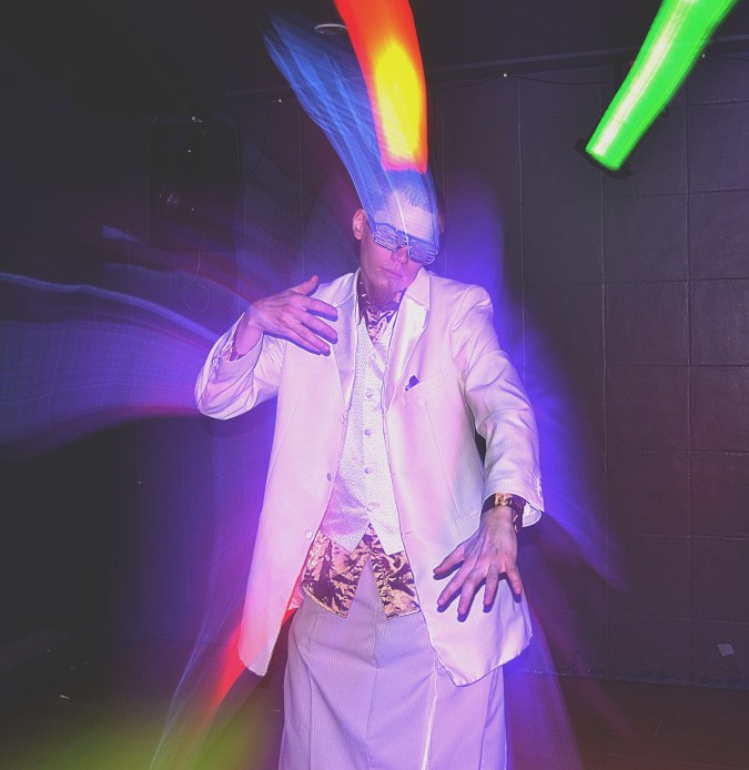 Tanssiva valkoiseen pukeutunut henkilö värivalojen loisteessa.