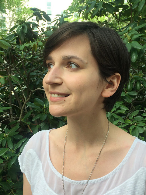 Alex Roberts katsoo vasemmalle kiinanruusu taustallaan valkoisessa paidassa, hymyilee.