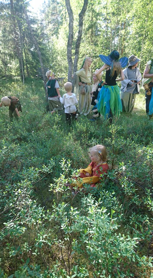 Pikkutyttö istuu mustikkamättäässä fantasiavaatteissa vähän etäällä muista.