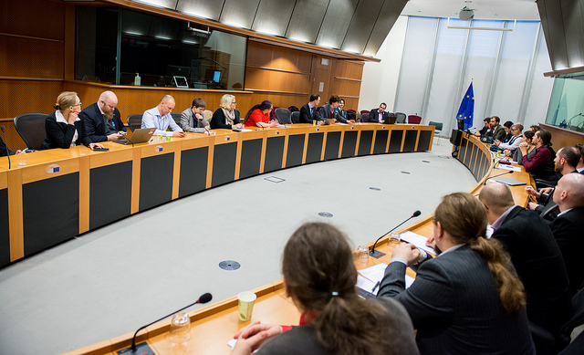 larppajat ja mepit istuvat kokoushuoneessa oikeassa Euroopan parlamentissa, EU:n lippu taka-alalla