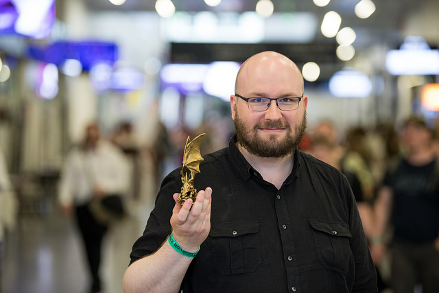 Juahna Pettersson Messukeskusksessa mustassa paidassa pitelee Kultainen lohikäärme patsasta ropecon ranneke ranteessaan