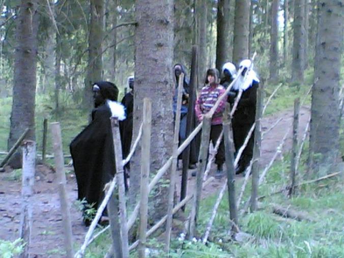 Kuvassa piemntohaltiat saattavat karvalakkista hahmoa tiellä.