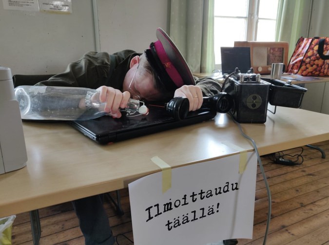 Koppalakkipäinen pelinjohtaja makaa läppärin kannen päällä unessa. Pöydän päässä on lappu "ilmoittaudu täällä!"