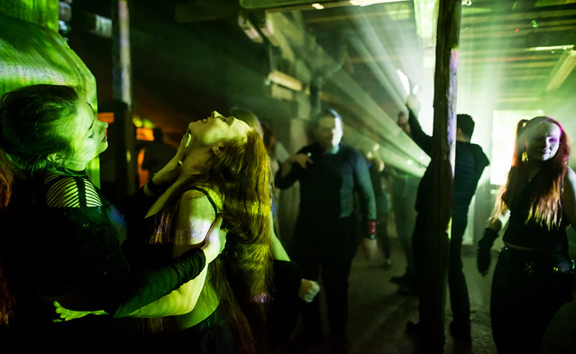 Strobo-valojen loisteessa tanssijoita, etuallalla sensuellisti tanssija hivelee naisen kaulaa.