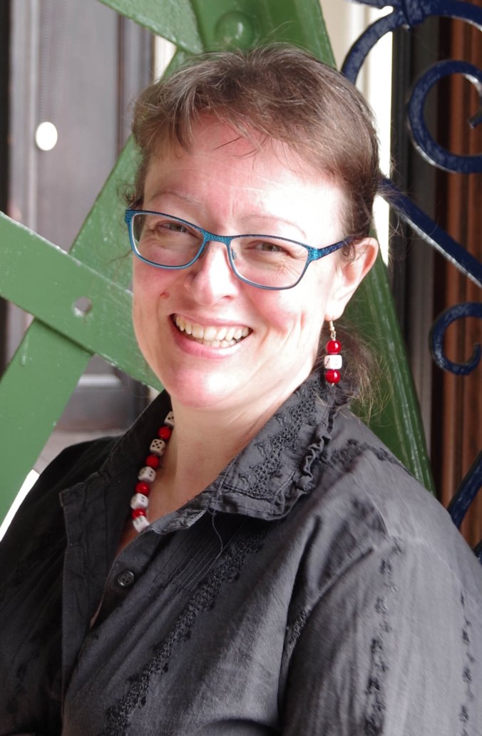 Kuvassa Lynne HArdy hymyilee, hänellä on ruskea tukka, sinisankaiset silmälasit, harmaa kauluspaita sekä puna-valkoiset korvakorut ja kaulakoru