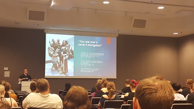 kuvassa ihmisiä salissa katsomassa esitelmää. Powerpointissa seinällä lukee "you are now a level 4 navigator"