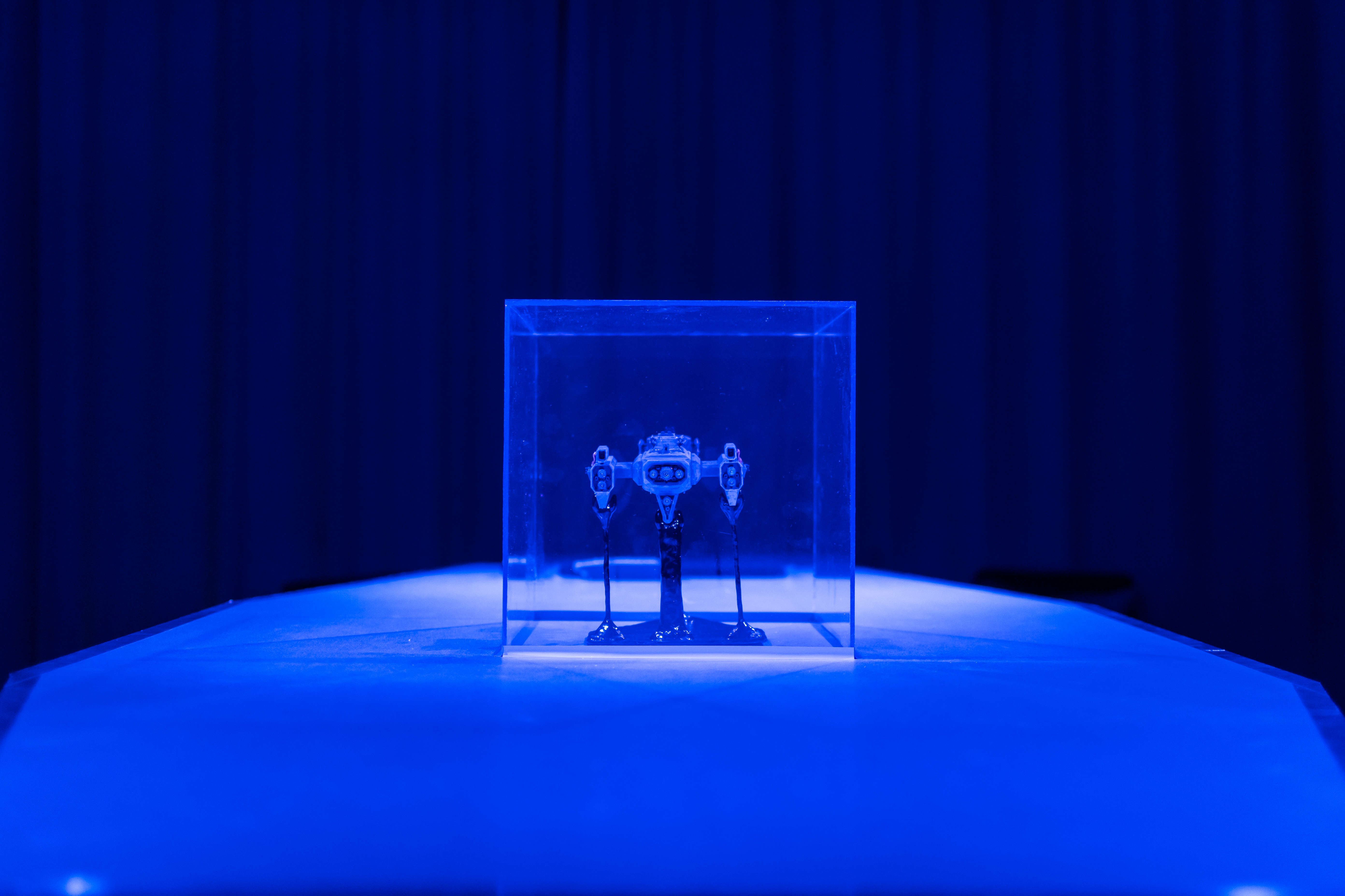 Kuvassa sinisessä valossa uusaluksen pienoimalli lasikuution sisässä.