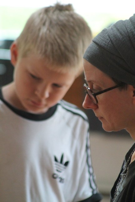 Kuvassa huivipäinen nainen opastaa nuorta poikaa jossain yhteisessä tehtävässä.