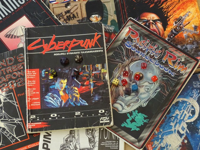 Kuvassa levitettynä CP2020 kuvitusta ja lähdeteoksia, sekä noppia.