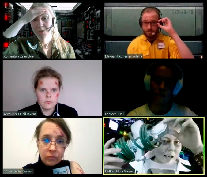 kuvassa kuuden videopuhelun ruudut, muutamalla takanaan virtuaalitausta, yksi pelaaja pitää käsissään mystistä laitetta ja esittelee sitä muille.