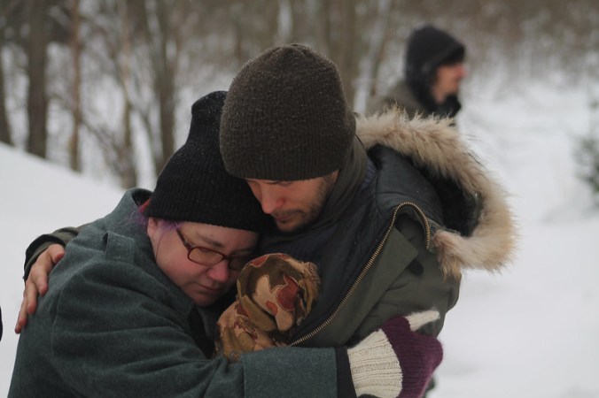 äiti ja isä halaavat rutistaen pientä vauvaa välissään, talvivaatteissaan hyisessä ulkoilmassa, lumen keskellä.
