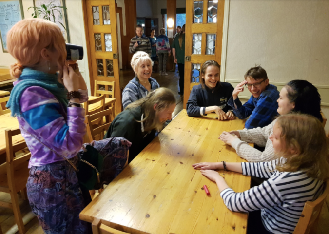 Kuvassa pöydän ääressä nauravia ihmisiä istumassa ja seisomassa.