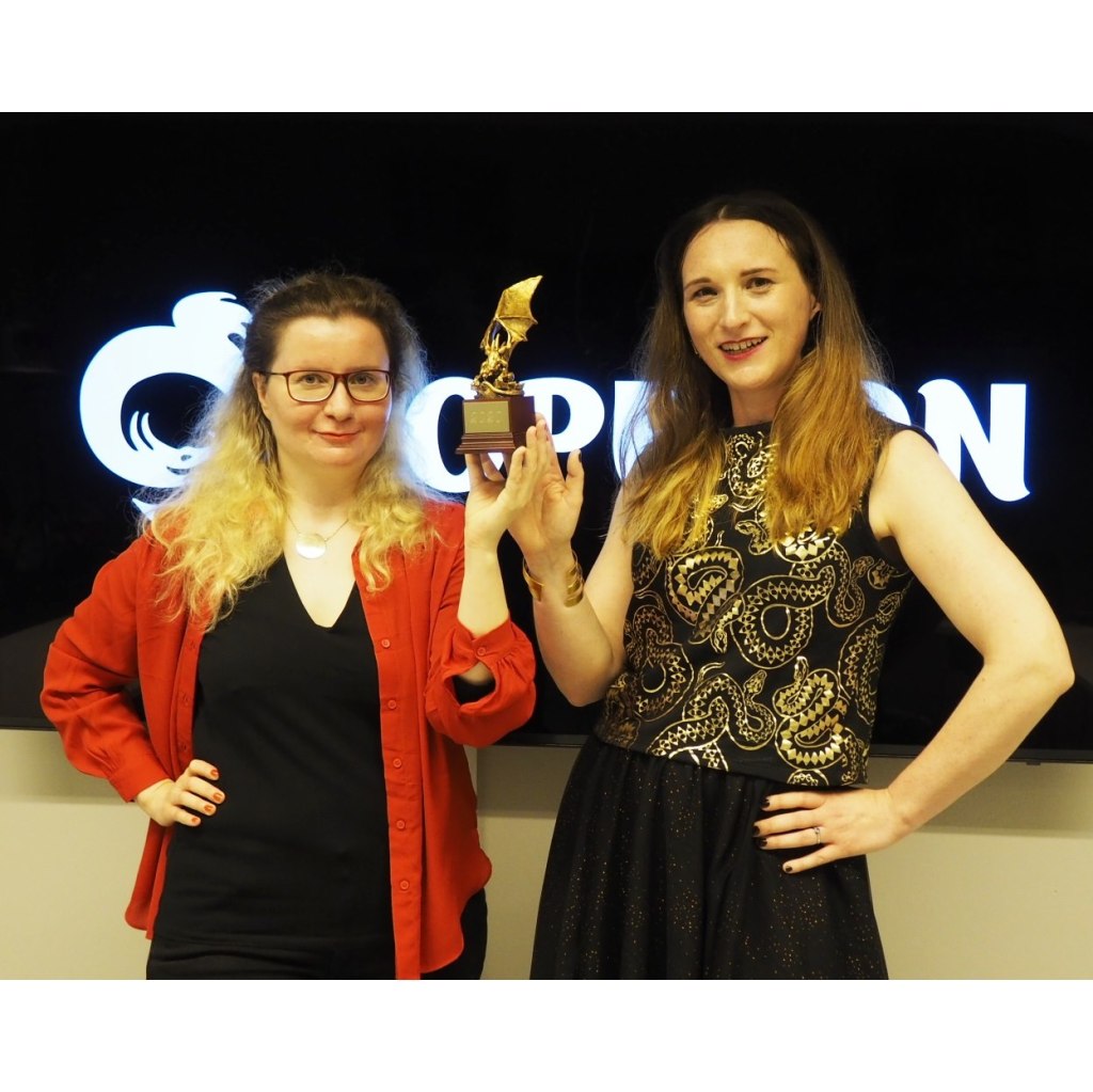 Kuvassa Laura Kalli ja Katri Lassila pitelevät kultainen lohikäärme patsasta. Takana Ropeconin logo.