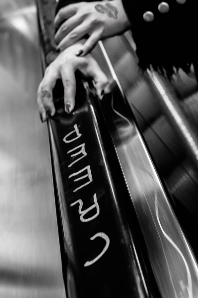 kuvassa kädet, joissa on lakatut pitkät kynnet, pitävät kiinni rullaportaiden kaiteesta, johon on kirjoitettu sana creep