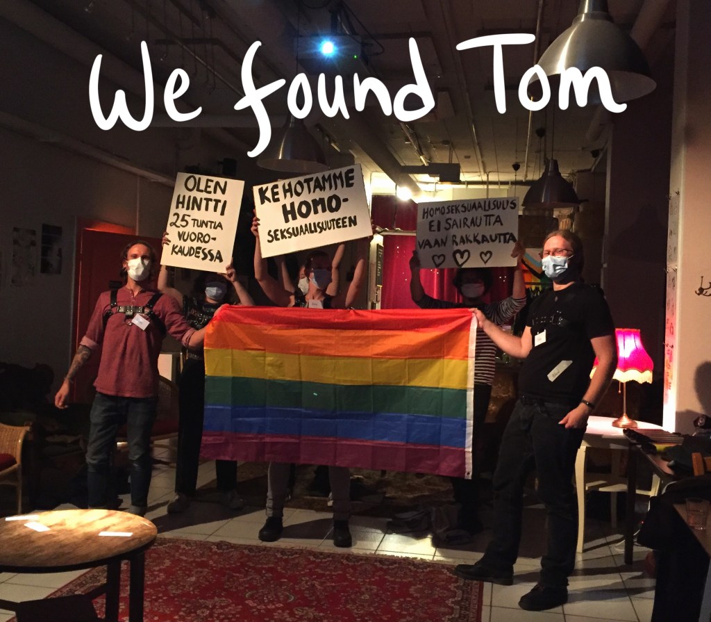 värikuva, jonka ylälaidassa lukee we found tom, kuvassa pelaajat kasvomaskit naamallaan ja nahkaremmit päällä esittävät mielenosoitusta, pitelevät sateenkaarilippua, ja kylttejä joissa olukee tekstejä kuten olen homo 25 tuntia vuorokaudessa ja kehotamme homoseksuaalisuuteen