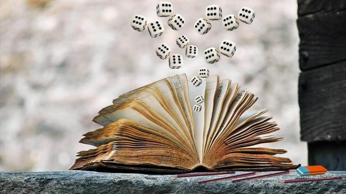 Kuvassa vanhan kirjan sivujen välistä lentää d6 noppia. Kirja lepää tasaisella kivellä, ja kivellä on myös lyijykyniä ja pyyhekumi.