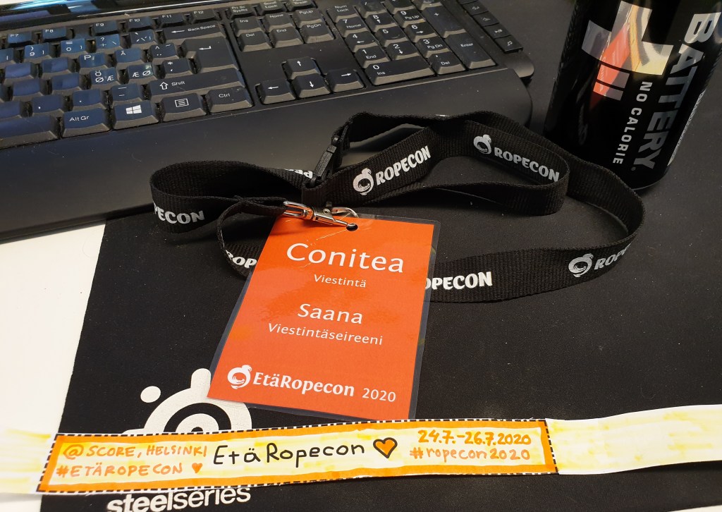 Kuvassa Saanan 2020 Ropecon badge sekä energiajuoma ja itse askarreltu Ropecon etä-ranneke vuodelle 2020.