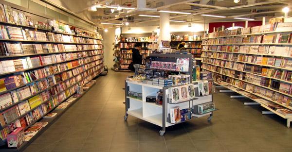 Kuva HelsinginFantasiapeleistä. Kuvassa on pitkät hyllyt ja niiden välissä pöytä täynnä myyntiartikkeleita.