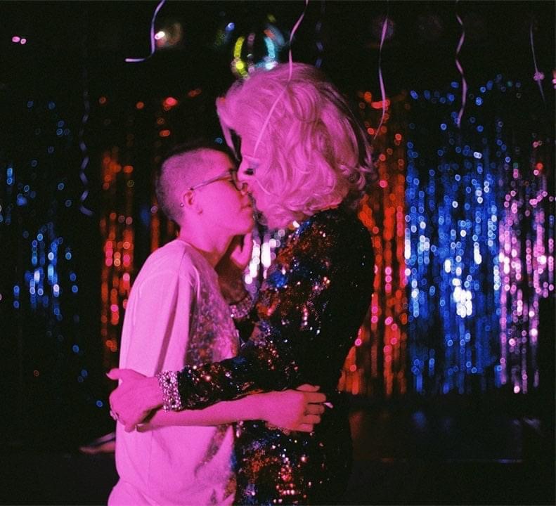 Kimaltelevan taustan edessä kaksi larppihahmoa tai pelaajaa suutelee ja halaa toisiaan hellästi. 