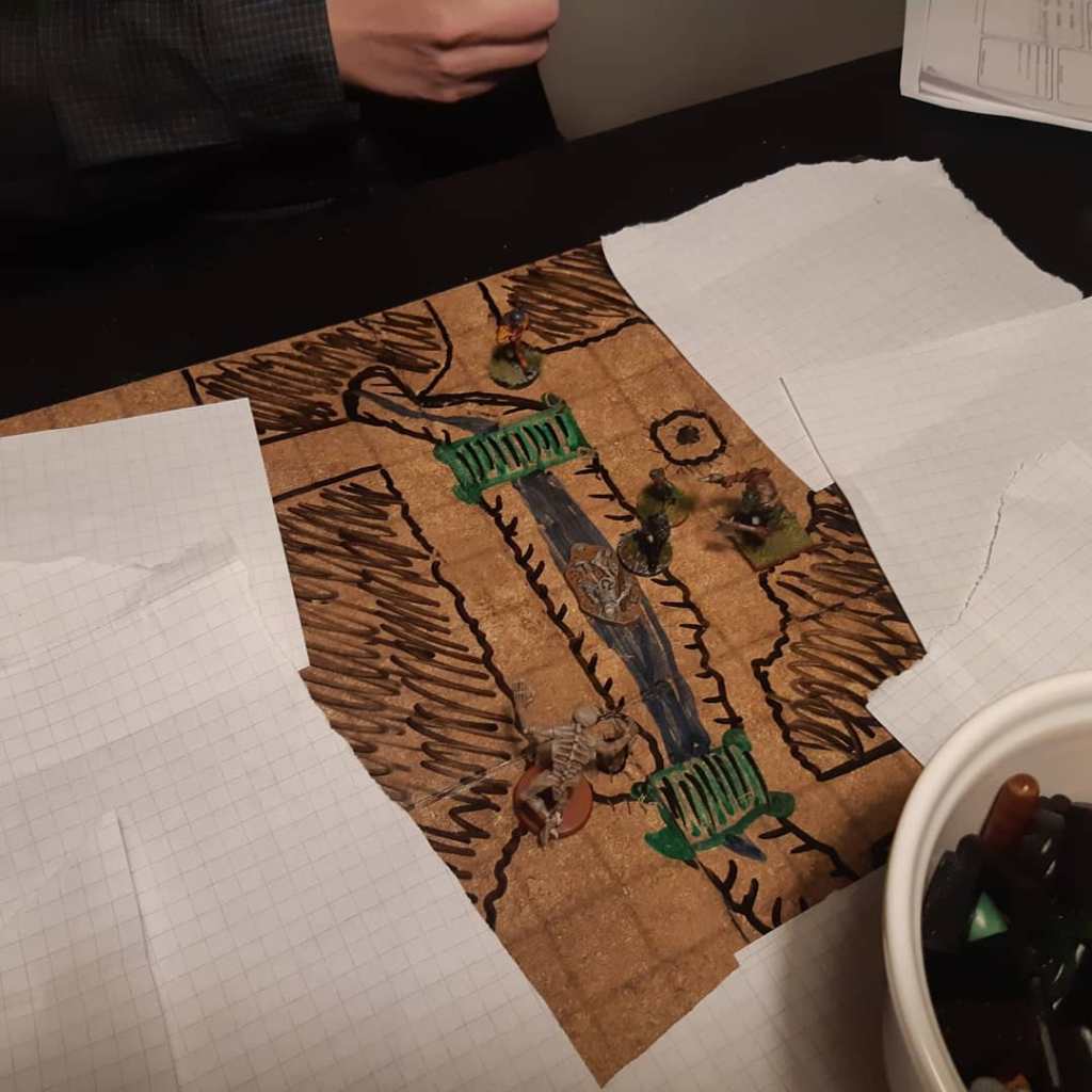 Käsin piirretty kartta, jonka päällä ovat pelaajahahmot ja luuranko miniatyyreinä.